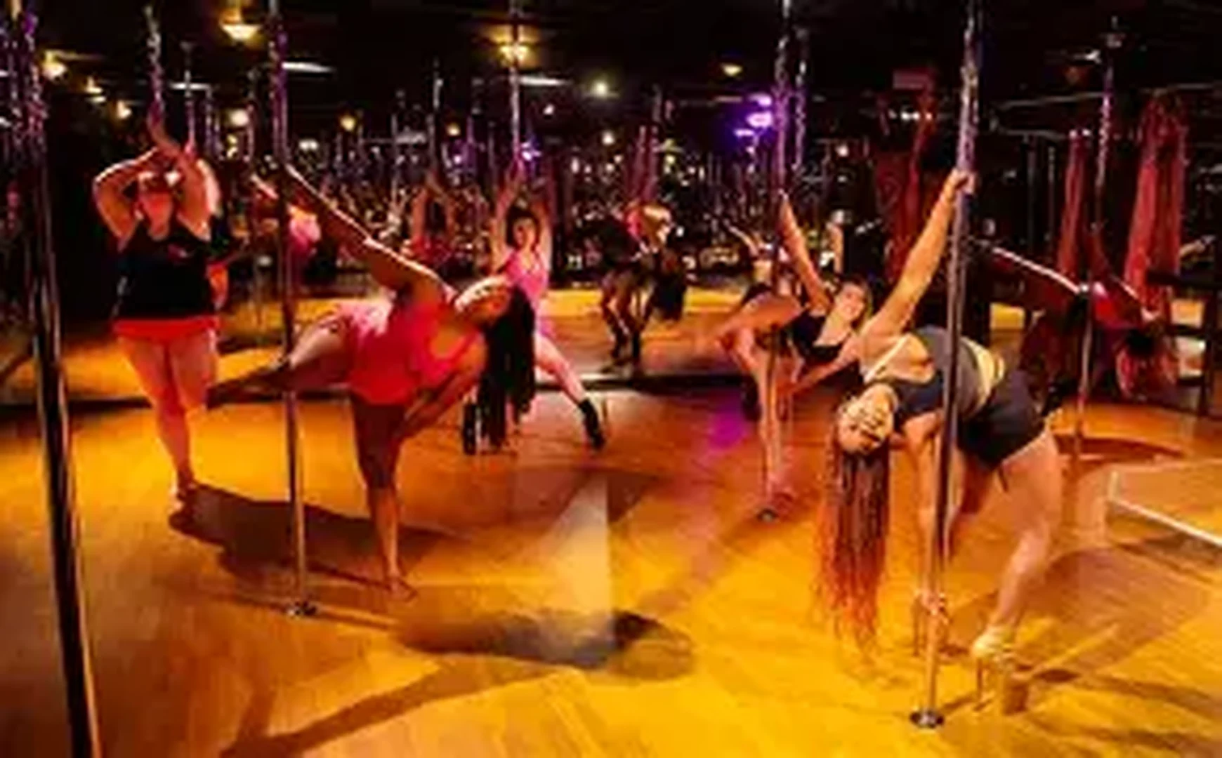Women practicing pole dancing in a mirrored studio with warm lighting
