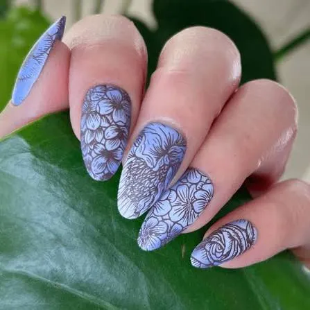 Blue almond nails with hand-painted floral artwork resting against a green leaf